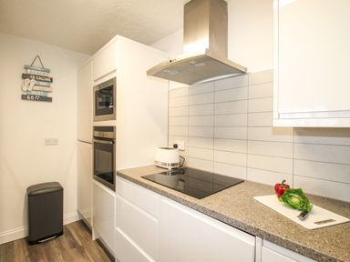 A kitchen with a black cooktop a toaster a cutting board with a pepper and lettuce and built-in oven and microwave at Brewers Retreat in Weymouth