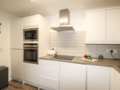 A kitchen with white cabinets a microwave and oven built in a column a toaster on the counter and a red pepper and lettuce on a cutting board on the counter at Brewers Retreat in Weymouth