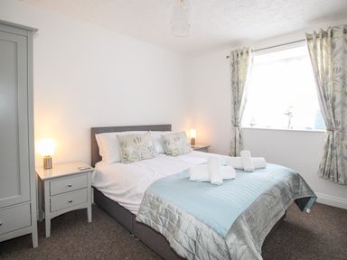 A bedroom with a double bed two bedside tables with lamps a wardrobe and a window with curtains at Brewers Retreat in Weymouth
