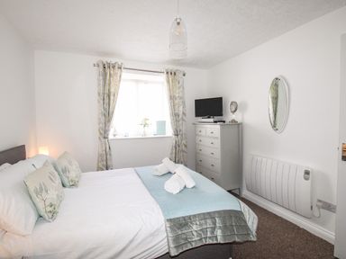 A bedroom with a bed, floral curtains, a chest of drawers with a TV on top, and a wall-mounted heater at Brewers Retreat in Weymouth