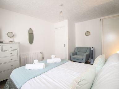A bedroom with a bed with rolled towels a blue armchair a white dresser and a door at Brewers Retreat in Weymouth