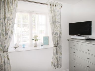 A window with patterned curtains and a white chest of drawers with a television on top at Brewers Retreat in Weymouth
