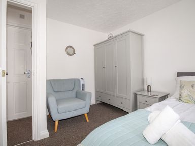 A bedroom with a grey wardrobe blue armchair bedside table and bed with white towels at Brewers Retreat in Weymouth