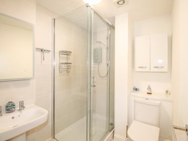 A bathroom with a glass shower enclosure a sink with a mirror and a toilet with a cabinet above it at Brewers Retreat in Weymouth