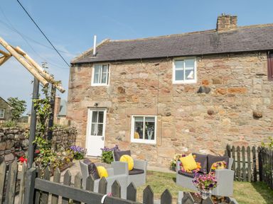 A stone cottage exterior with outdoor seating area and flowers at O'Neil Cottage in Beadnell