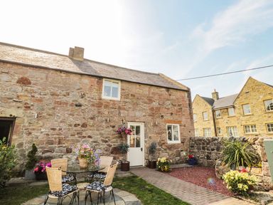 A stone cottage exterior with a small patio table and chairs surrounded by flower pots at O'Neil Cottage in Beadnell