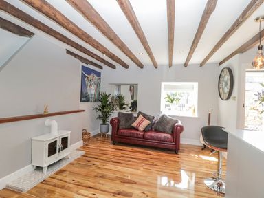 A living room with a red leather sofa wooden beams on ceiling a white stove and a large clock on the wall at O'Neil Cottage in Beadnell