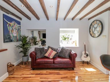 A living room with a red leather sofa and cushions a guitar large wall clock plants wooden beams on ceiling and artwork at O'Neil Cottage in Beadnell