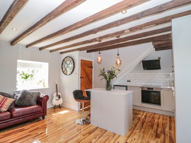 A kitchen and living area with wooden ceiling beams a red sofa a guitar a clock and a kitchen island at O'Neil Cottage in Beadnell
