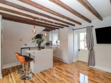 A kitchen with wooden beams on the ceiling a white island with two chairs and a vase of flowers at O'Neil Cottage in Beadnell