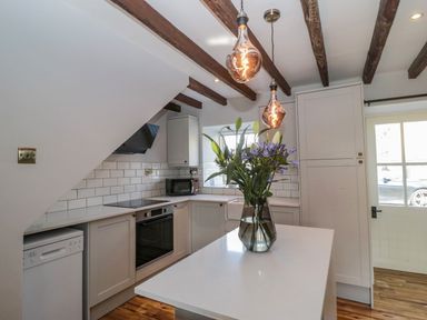 A kitchen with wooden ceiling beams white cabinets a countertop island with flowers and pendant lights at O'Neil Cottage in Beadnell