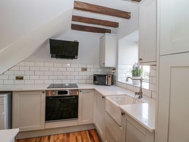 A kitchen with white cabinets a black oven a microwave a farmhouse sink and exposed wooden ceiling beams at O'Neil Cottage in Beadnell