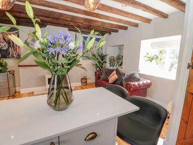 A living room with a vase of flowers on a white table black chairs a red sofa with pillows wooden ceiling beams and colorful artwork on the walls at O'Neil Cottage in Beadnell