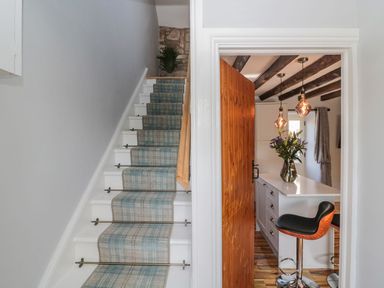 A staircase with a plaid carpet runner next to a doorway showing a kitchen island with flowers and bar stools at O'Neil Cottage in Beadnell