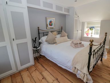 A bedroom with a metal bed frame white bedding pillows folded towels wooden floor and built in cupboards at O'Neil Cottage in Beadnell