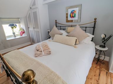 A bedroom with a bed with beige pillows and folded towels on it a small window with flowers and cushions and a bedside table with a lamp at O'Neil Cottage Beadnell