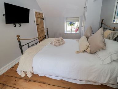 A bedroom with a bed with beige pillows and folded towels a wooden door a wall mounted tv and a window with flowers at O'Neil Cottage in Beadnell