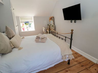 A bedroom with a metal bed frame pillows towels on bed a wall mounted TV and a window with flowers at O'Neil Cottage in Beadnell