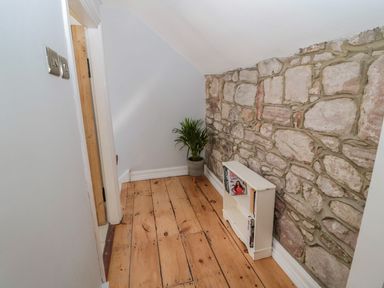 A small hallway with a stone wall a wooden floor a white bookshelf and a potted plant at O'Neil Cottage in Beadnell