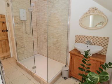 A bathroom with a walk-in shower wooden cabinet with sink and decorative mirror at O'Neil Cottage Beadnell