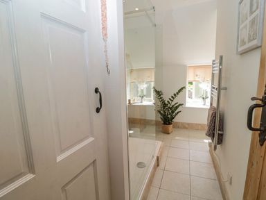 A bathroom with a glass shower enclosure a plant on the floor a towel on a wall-mounted rack and windows with blinds at O'Neil Cottage in Beadnell
