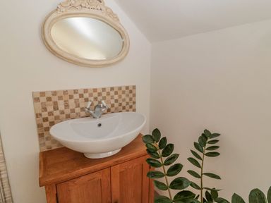 A bathroom sink with a checkered tile backsplash a decorative mirror above and a plant below at O'Neil Cottage in Beadnell