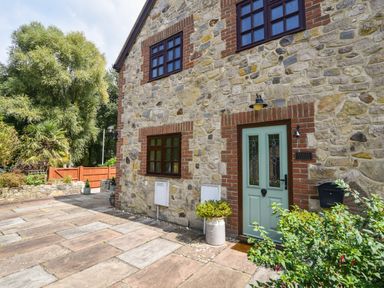 Front entrance of a stone cottage with a light green door and brick accents at Barley Cottage in Weycroft near Axminster