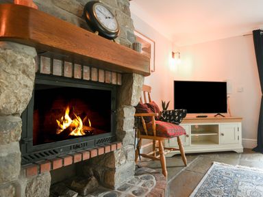 A living room with a stone fireplace fire burning a wooden rocking chair with cushions a television on a stand and a rug on the floor at Barley Cottage Weycroft near Axminster