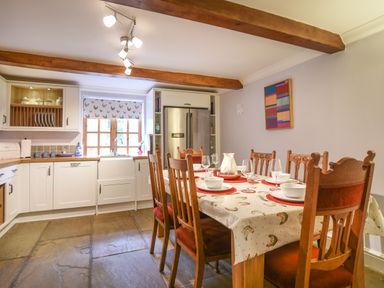 A kitchen with wooden beams a dining table set with plates and glasses and a refrigerator at Barley Cottage in Weycroft near Axminster