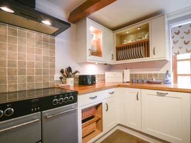A kitchen corner with white cabinets wooden countertop cooking utensils and a stove at Barley Cottage in Weycroft near Axminster