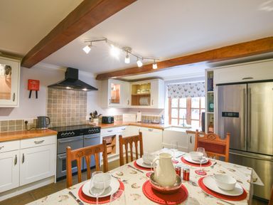 A kitchen with wooden beams a dining table set for four a stove a refrigerator and cabinets at Barley Cottage in Weycroft near Axminster