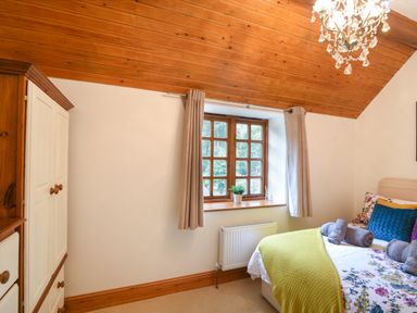 A bedroom with a double bed with floral bedding and yellow blanket next to a window with curtains and a wardrobe at Barley Cottage Weycroft near Axminster