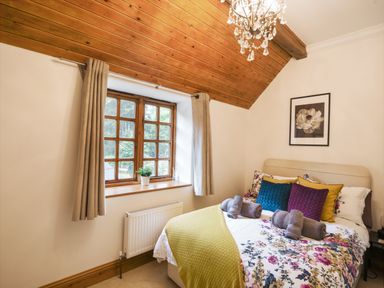 A bedroom with floral bedspread colorful pillows and rolled towels by a wooden window at Barley Cottage Weycroft near Axminster