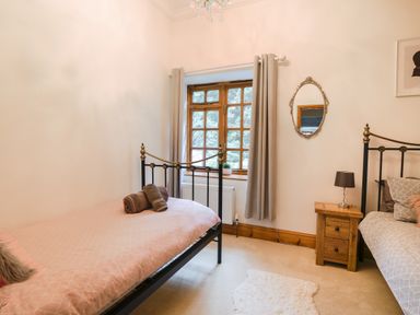 A bedroom with two single metal beds a wooden window with curtains a wooden nightstand and a wall mirror at Barley Cottage Weycroft near Axminster