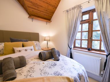 A bedroom with a bed and pillows next to a window with curtains and a lamp at Barley Cottage Weycroft near Axminster