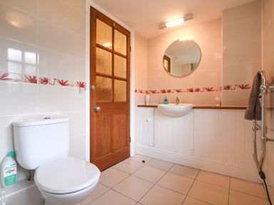 A bathroom with a toilet a wooden door a circular mirror a sink and a towel rack at Barley Cottage in Weycroft near Axminster