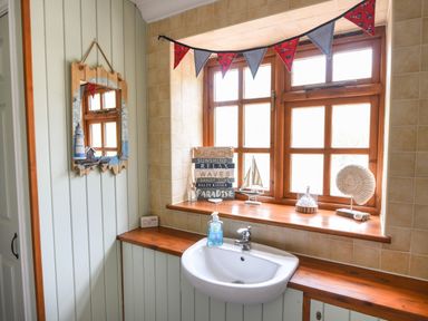 A bathroom with a white sink wooden window sill nautical decorations and a mirror at Barley Cottage in Weycroft near Axminster