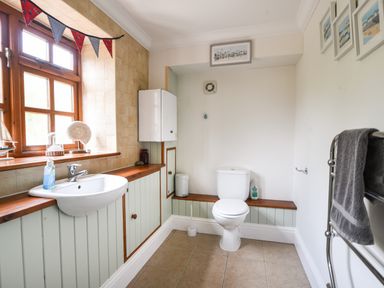 A bathroom with a white sink and toilet wooden window and towels on a rack at Barley Cottage in Weycroft near Axminster