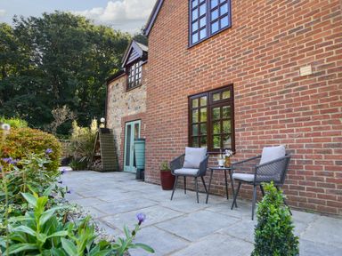 An outdoor patio area with two chairs and a small table against a brick and stone house with garden plants at Barley Cottage Weycroft near Axminster