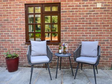 Two chairs with cushions and a small table with wine and glasses outside a brick wall with a window at Barley Cottage in Weycroft near Axminster