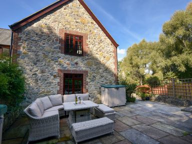 An outdoor patio with wicker seating and a table next to a stone house at Barley Cottage in Weycroft near Axminster