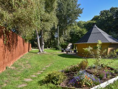 A garden with flower beds and a wooden cabin with outdoor furniture at Barley Cottage Weycroft near Axminster
