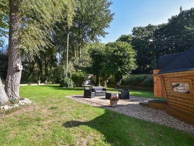 An outdoor garden area with patio furniture a flower pot a wooden cabin and trees at Barley Cottage in Weycroft near Axminster