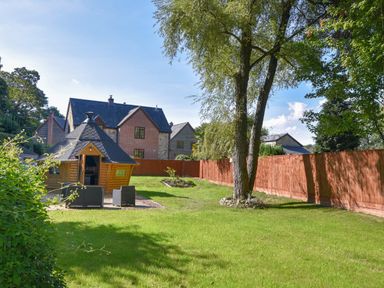 A garden with a tree a small cabin and outdoor seating in front of houses at Barley Cottage in Weycroft near Axminster