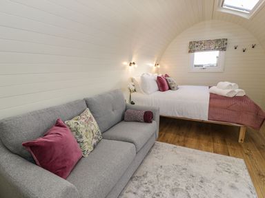 A bedroom with a gray sofa a bed with white linens and pillows a window and wooden floor at Yr Onnen in Bontuchel near Ruthin