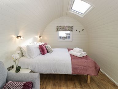 A bedroom with a double bed with white and pink bedding a grey chair and a small window at Yr Onnen in Bontuchel near Ruthin