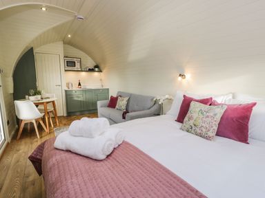 A bedroom with a bed with pink pillows and towels a gray sofa a small dining table and kitchenette at Yr Onnen in Bontuchel near Ruthin