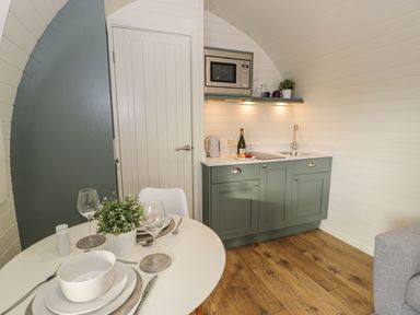 A small kitchen with green cabinets a microwave sink and a table set with plates glasses and a plant at Yr Onnen Bontuchel near Ruthin