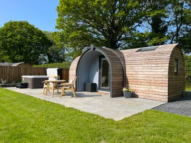 A small wooden pod with an outdoor seating area and a hot tub on a paved patio at Yr Onnen in Bontuchel near Ruthin