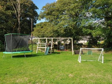 A backyard with a trampoline, a wooden playset with swings and a slide, and a small soccer goal at Trelawney in Mawnan Smith Near Falmouth
